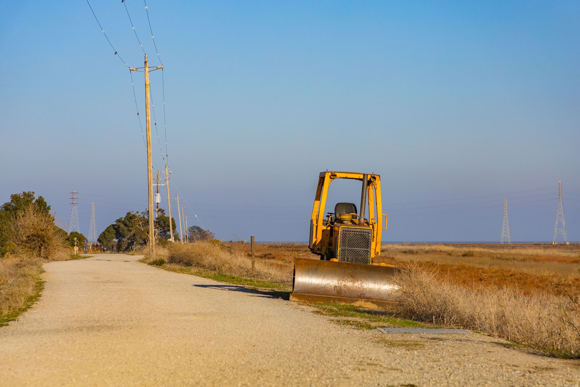 Yellow bulldozer parked on a rural road beside electrical poles under a clear blue sky.