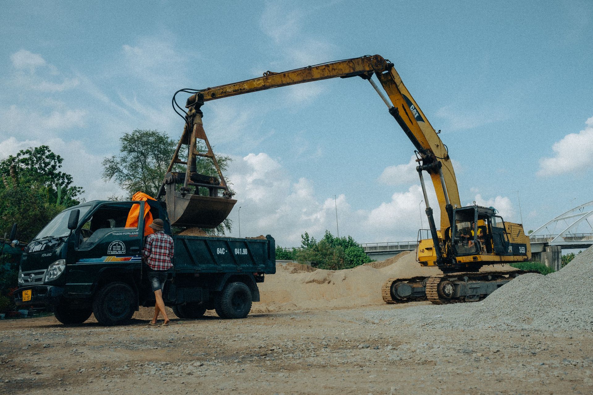 Excavator and truck on a construction site in Vinh Long, Vietnam, under a clear sky.
